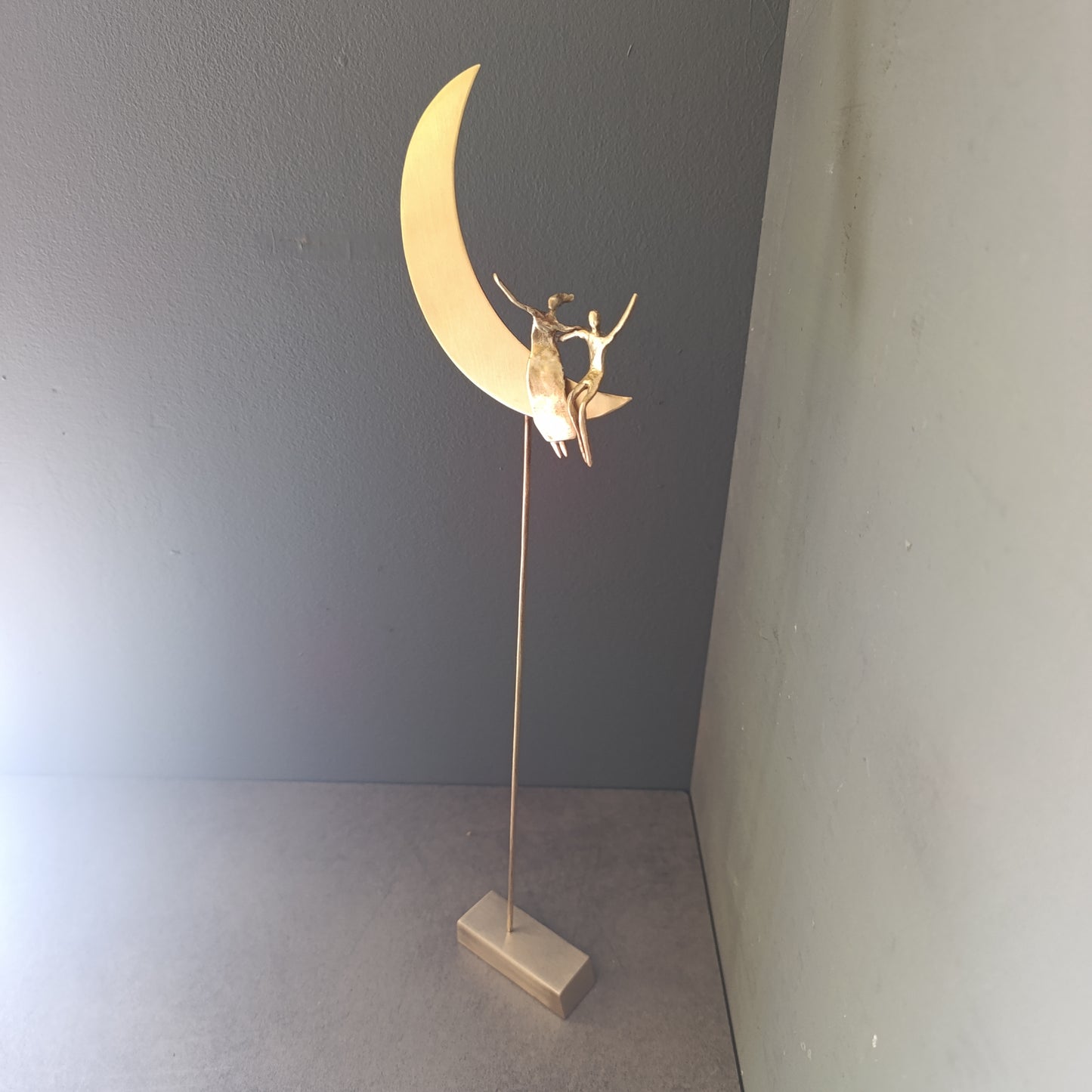 Bronze sculpture of a figure on a crescent moon against a gray wall.